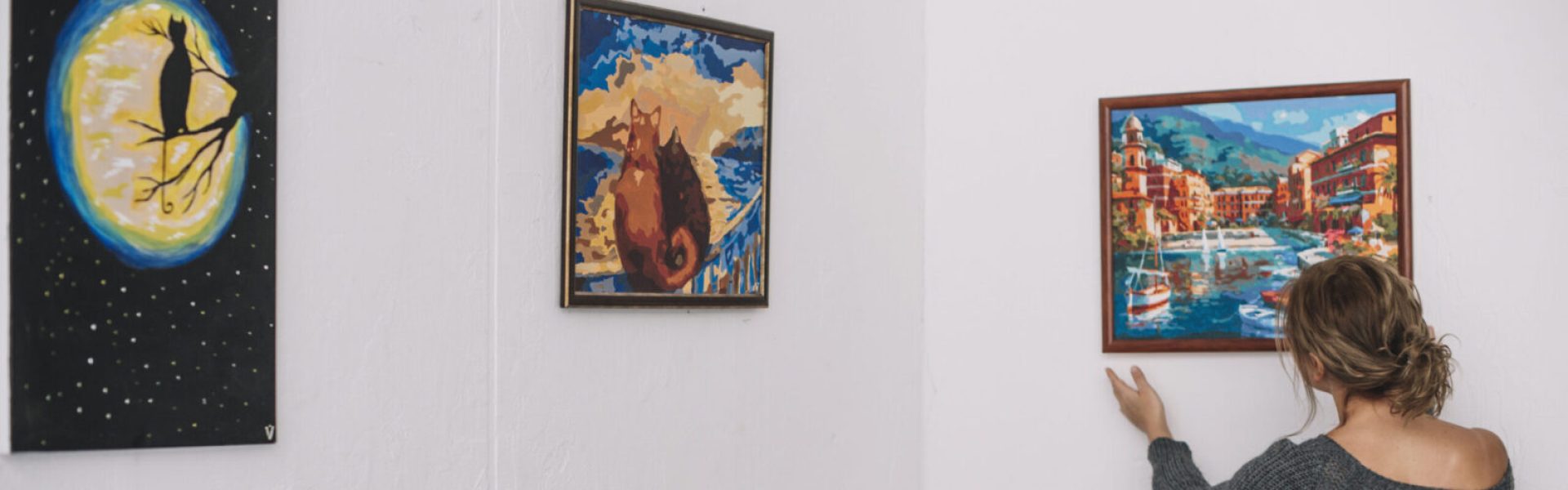 kobieta umieszcza obrazek na scianie